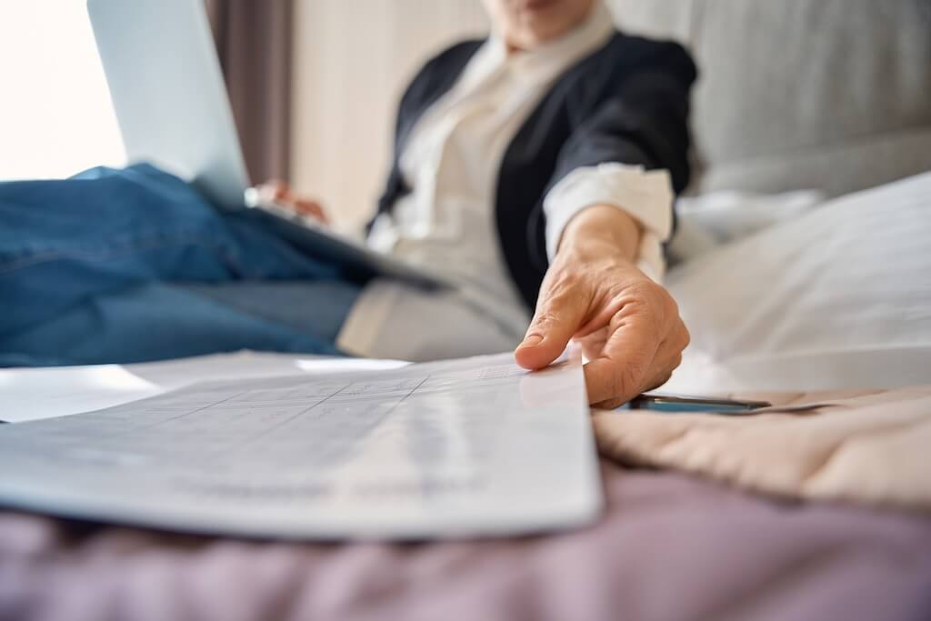 Businesswoman holding reports documents working with laptop while sitting in hotel room